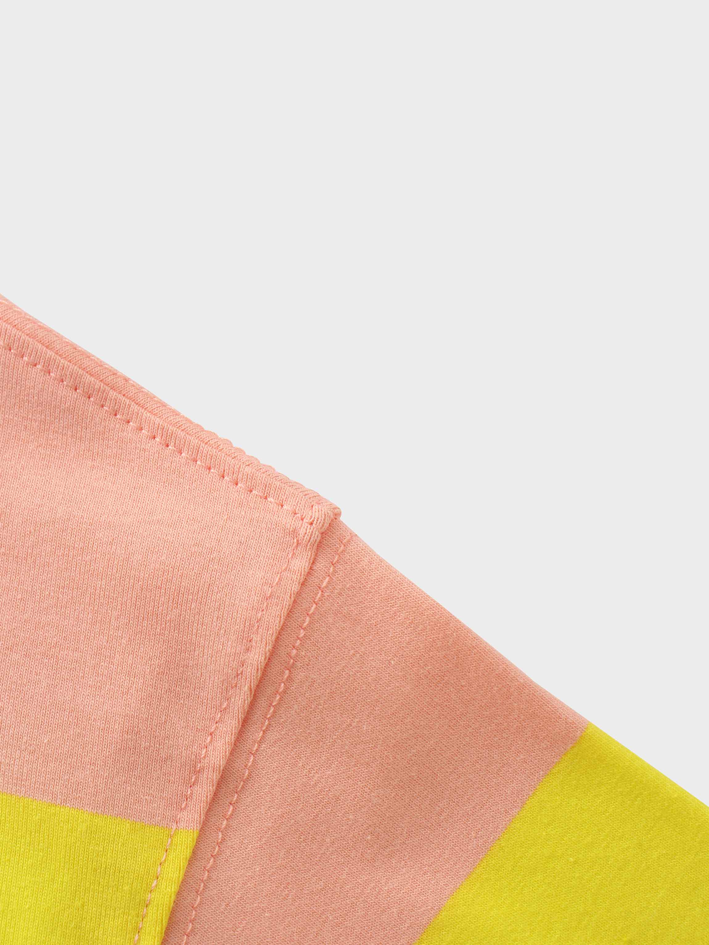 A close-up of a color-blocked garment. The image shows a seam where a panel of light pink fabric is joined with panels of yellow and tan fabric.