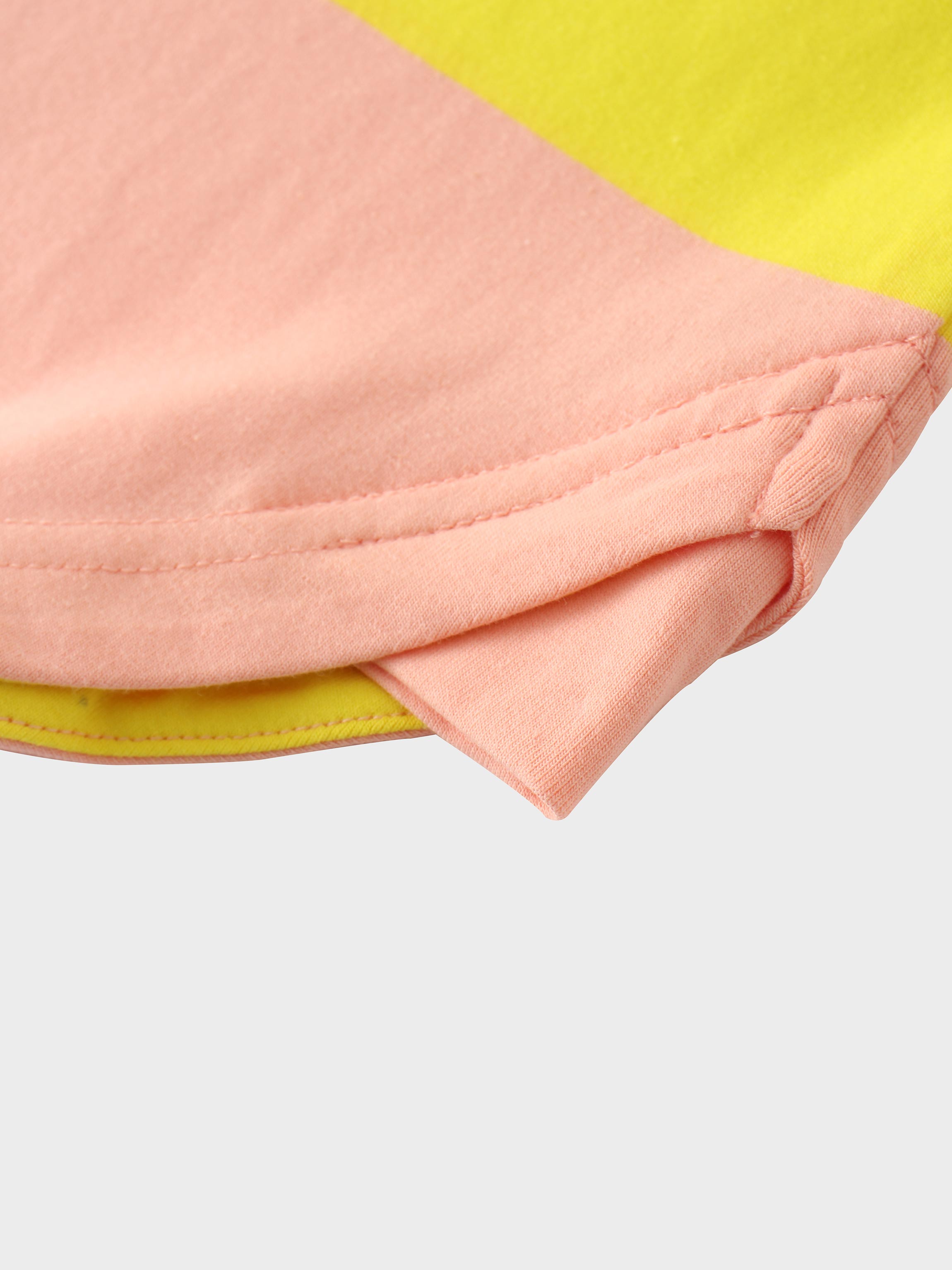 A close-up view of the bottom hem of the color-blocked shirt. The image shows where the yellow front panel and the pink back panel are joined at the side, both finished with a neat, double-stitched hem.