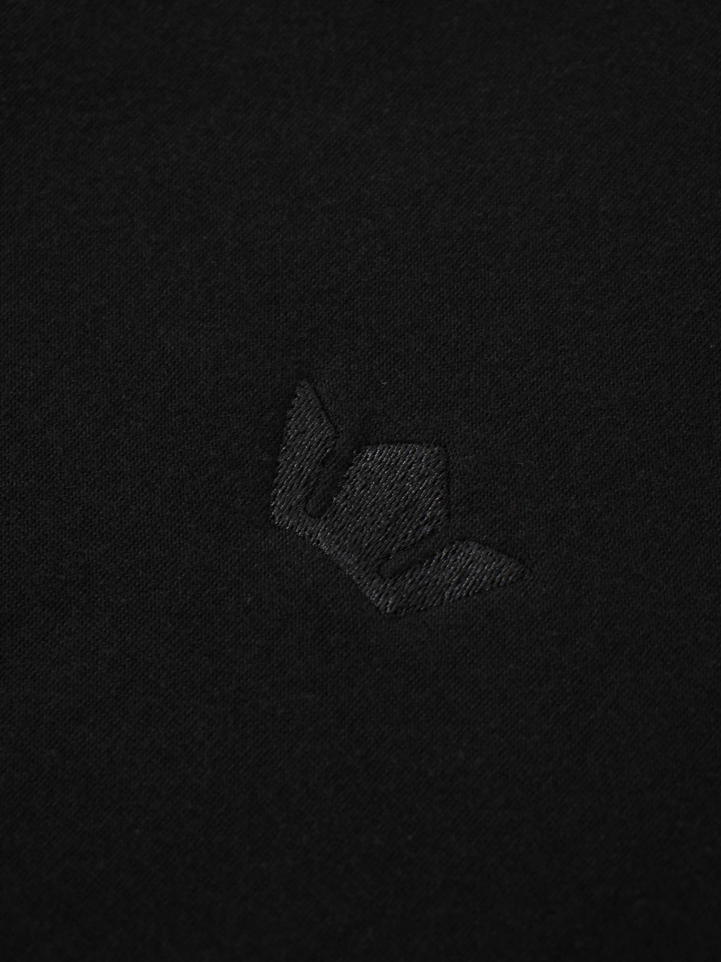 A macro shot of the black fabric, featuring a small, embroidered logo. The logo is stitched with matching black thread, creating a subtle, black-on-black effect.
