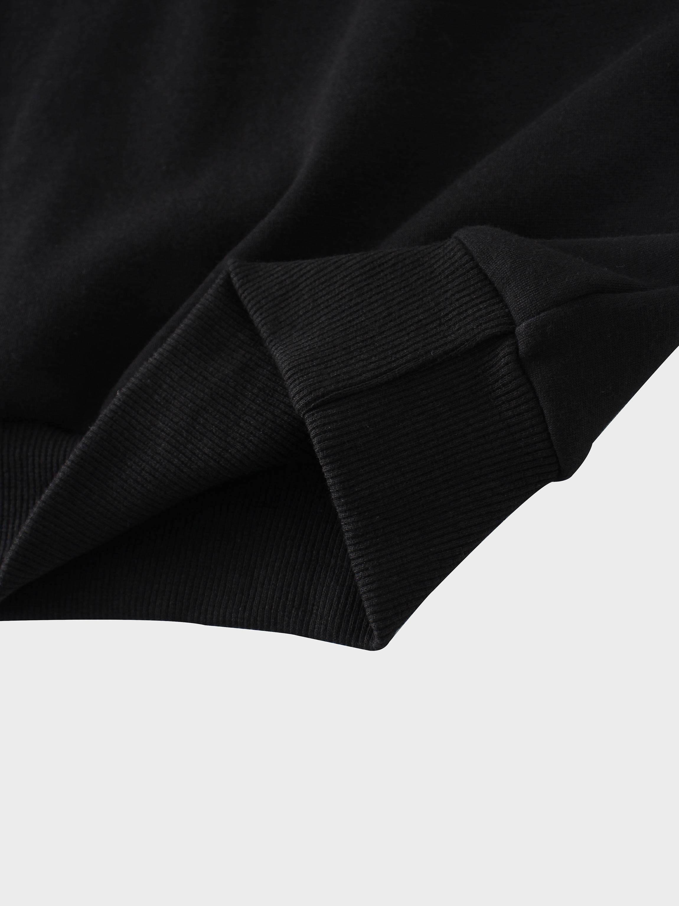 A close-up of the thick, ribbed cuff or bottom hem of a black sweatshirt. The ribbed band is attached to the smooth fabric of the main garment.