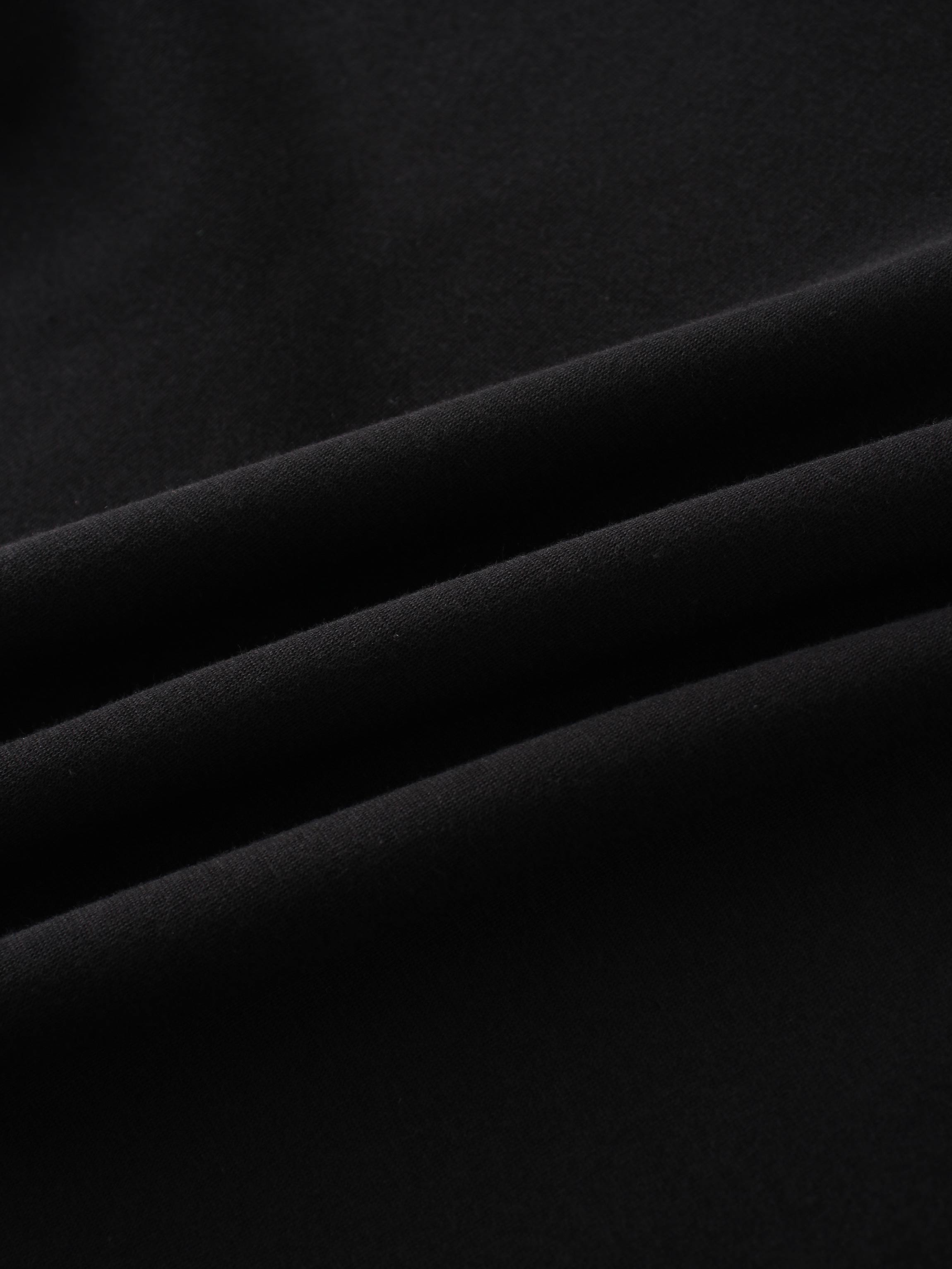 A close-up of a smooth, black fabric. The material is arranged in soft, diagonal folds, with lighting creating highlights on the creases.