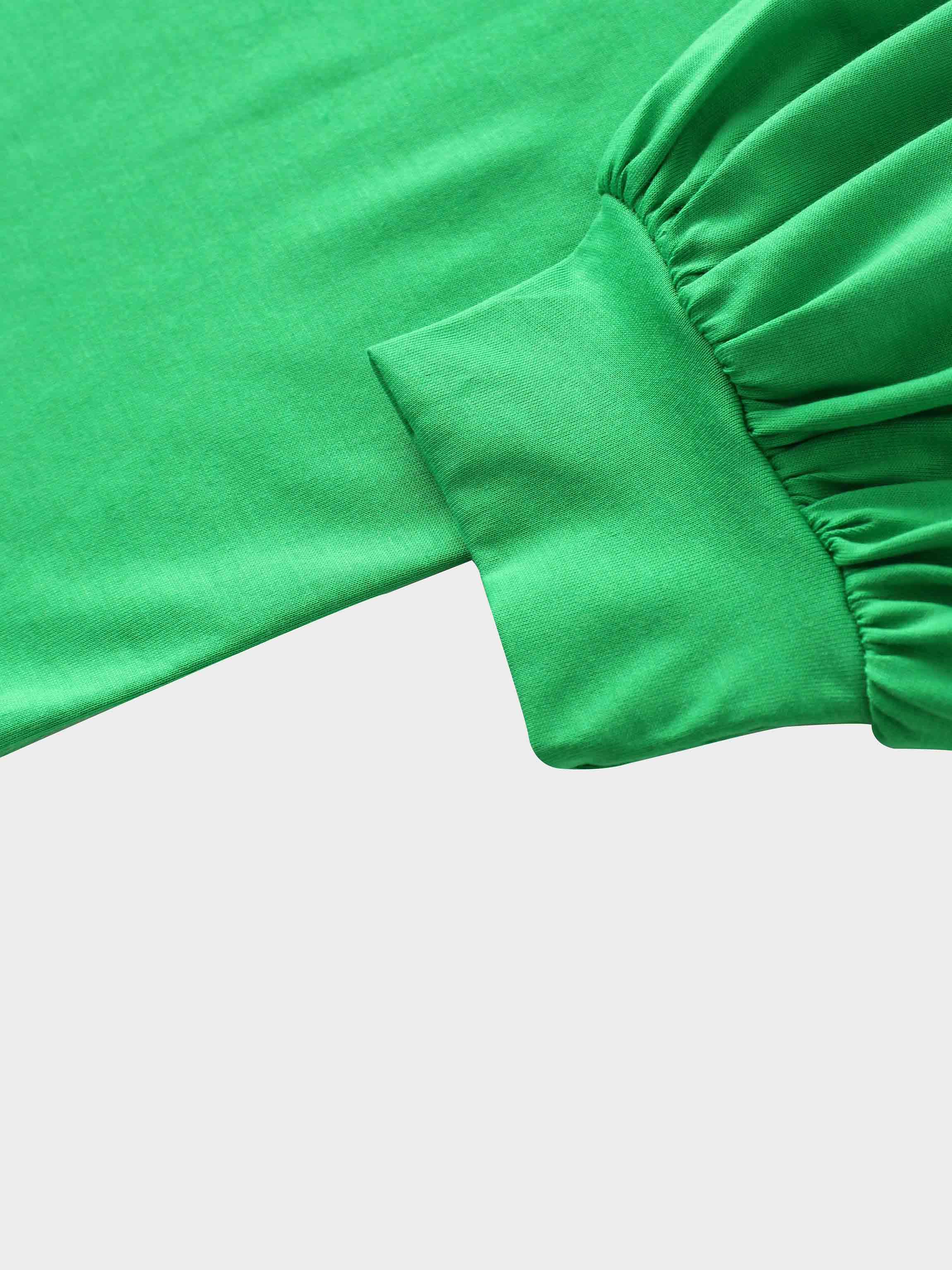 A close-up of the sleeve of the vibrant green garment. The main fabric is gathered where it attaches to a wide, smooth cuff at the wrist.
