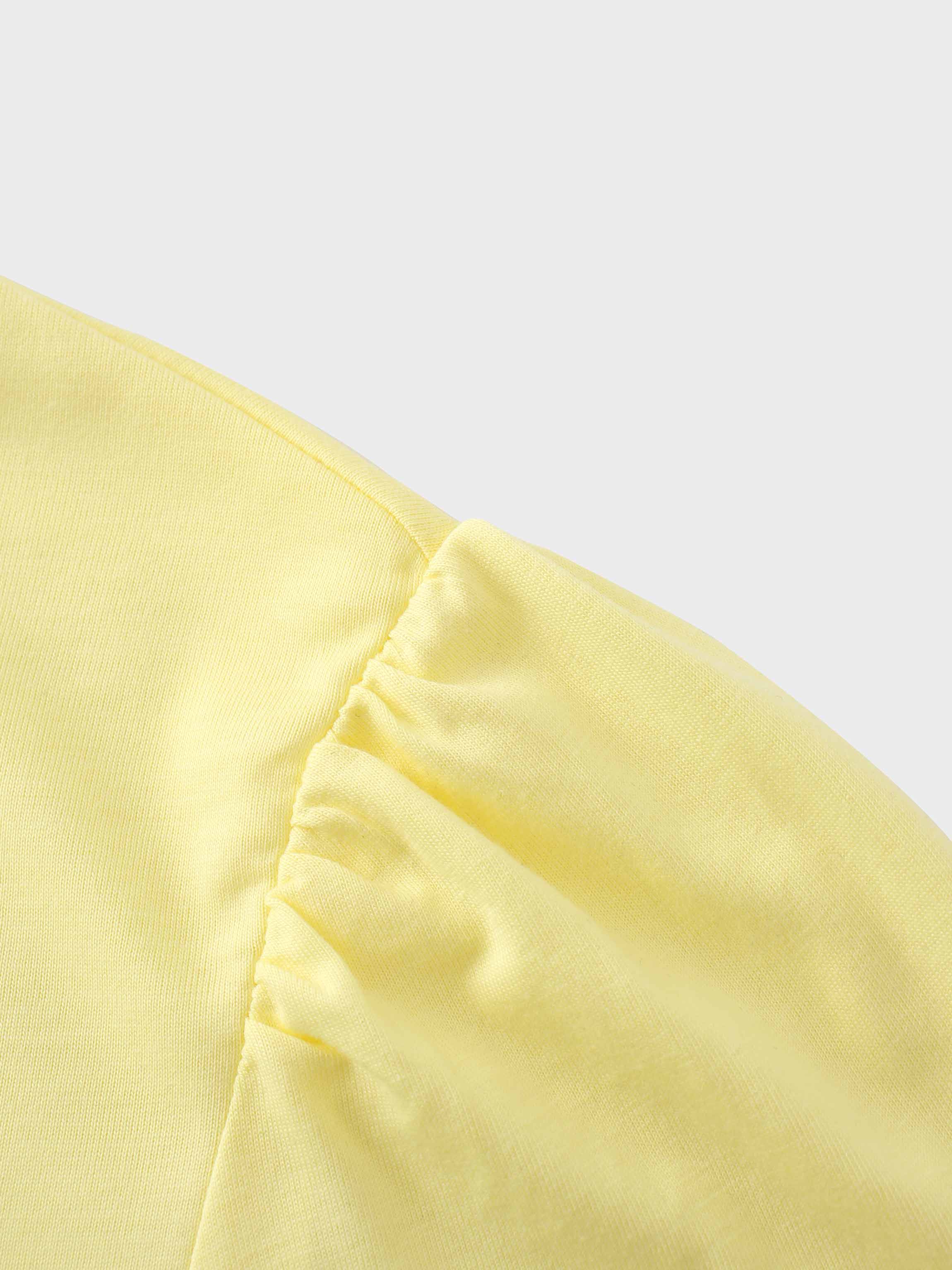 A close-up of the shoulder of the pale yellow shirt. The fabric at the top of the sleeve is gathered where it is sewn into the shoulder, creating a puff sleeve detail.