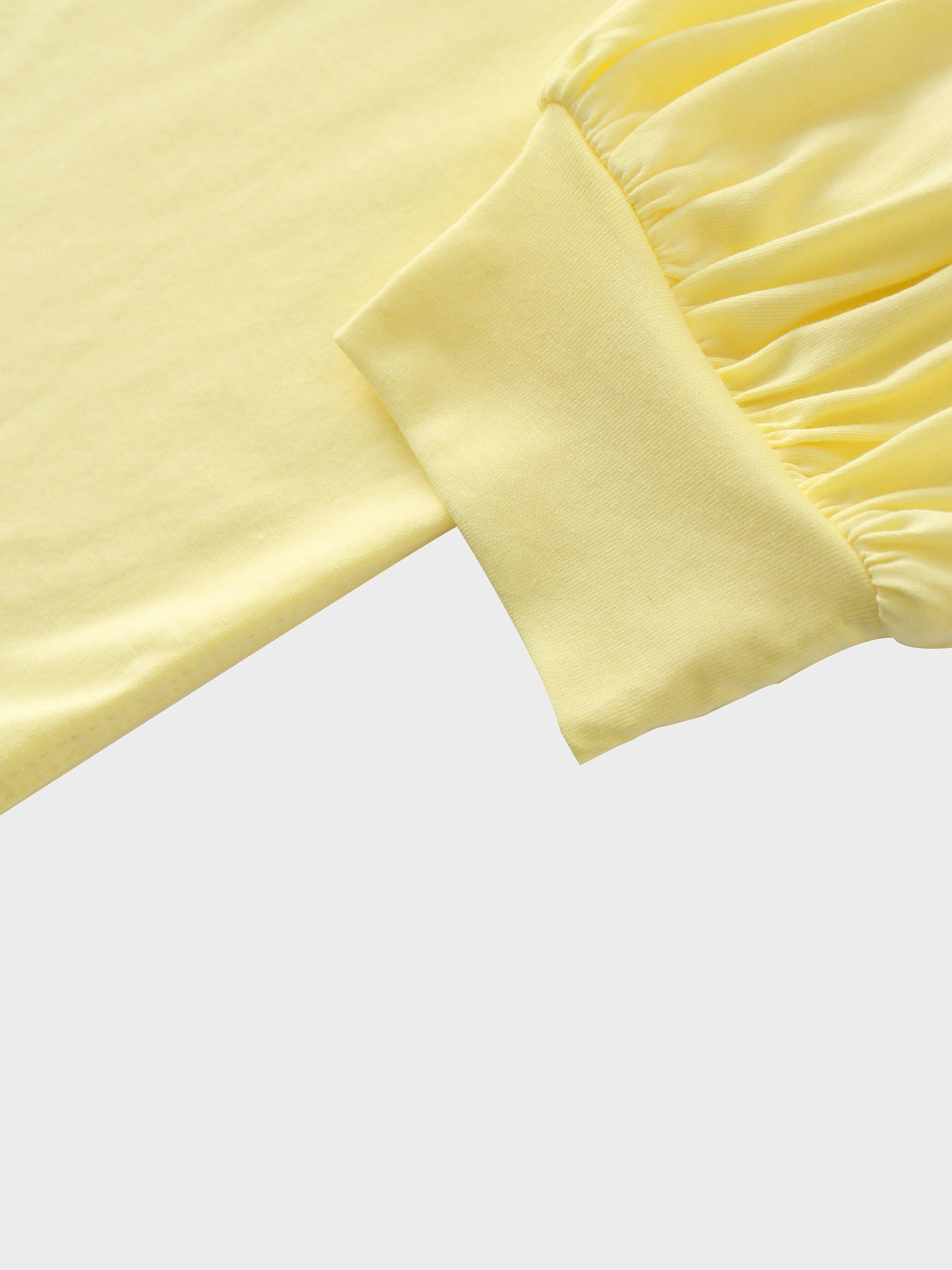A close-up of the sleeve of the pale yellow garment. The main fabric is gathered where it attaches to a wide, smooth cuff at the wrist.