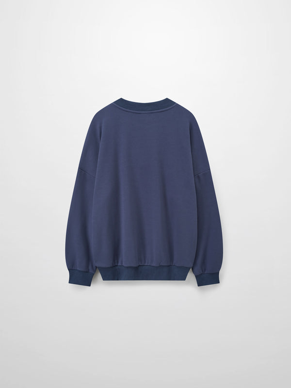 A full, front view of the dusty-blue sweatshirt. It has a ribbed crewneck collar, cuffs, and bottom hem, with the small, tone-on-tone embroidered logo visible on the left chest.