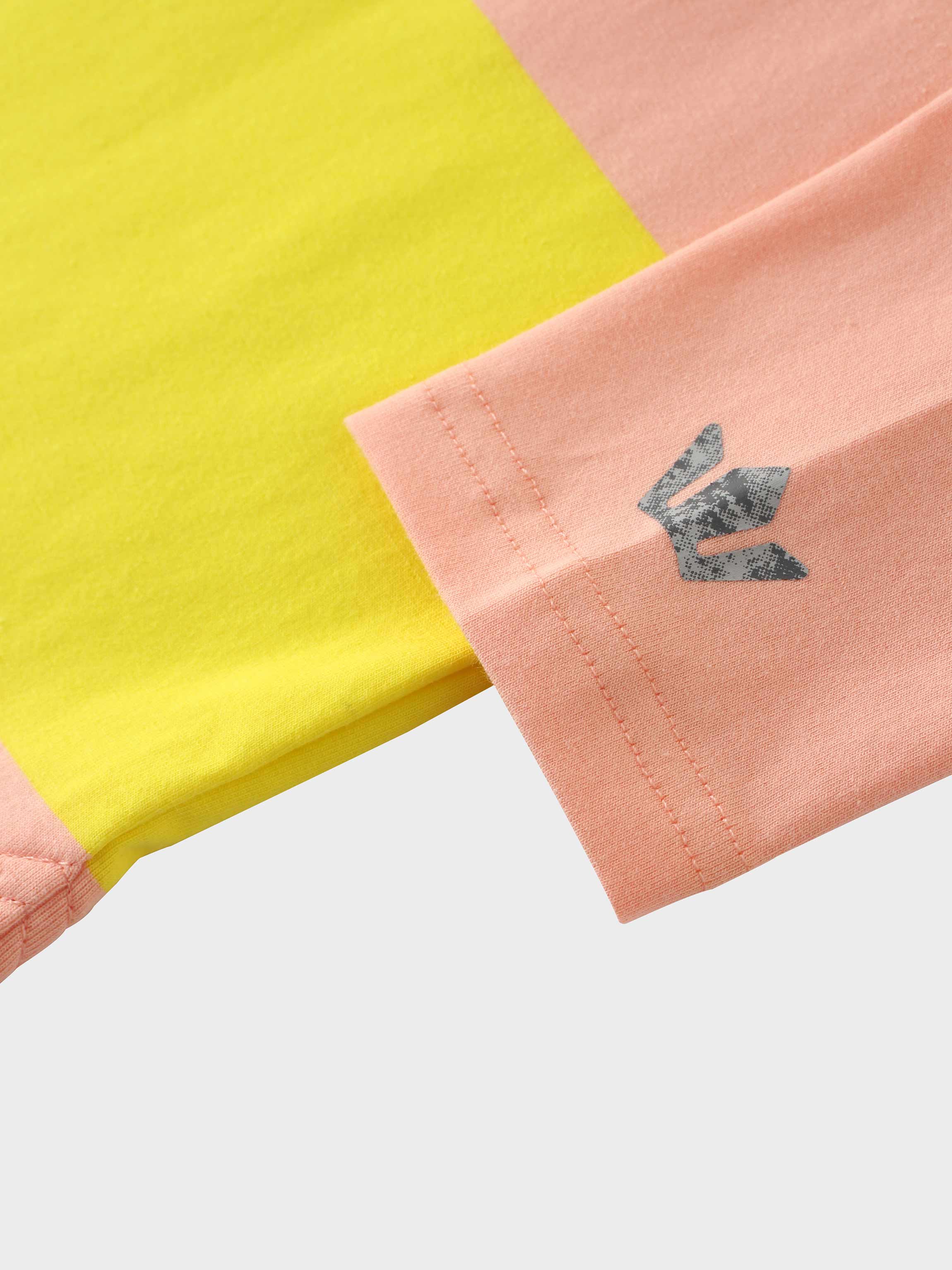 A close-up of the sleeve on the color-blocked shirt. The cuff is made of pink fabric and has a dark gray, textured logo printed on it, seen here next to the yellow fabric of the shirt&