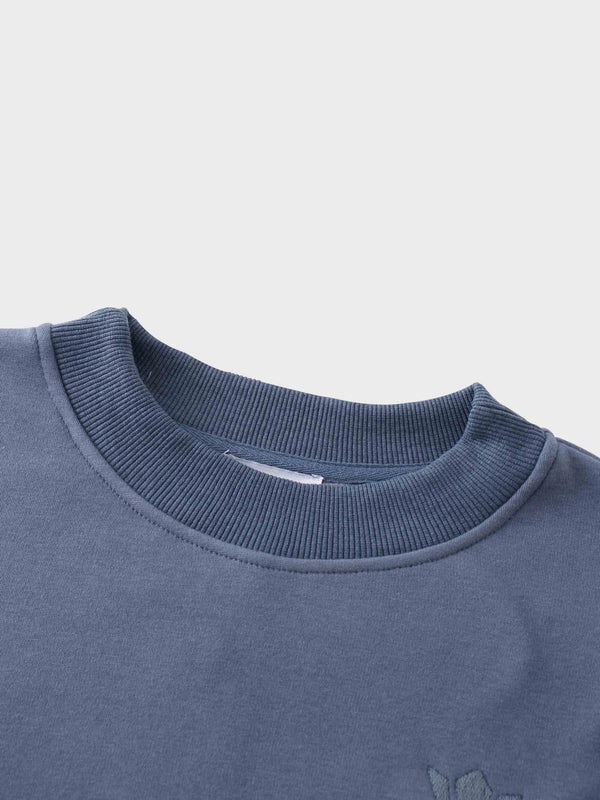 A full, front view of the dusty-blue sweatshirt. It has a ribbed crewneck collar, cuffs, and bottom hem, with the small, tone-on-tone embroidered logo visible on the left chest.