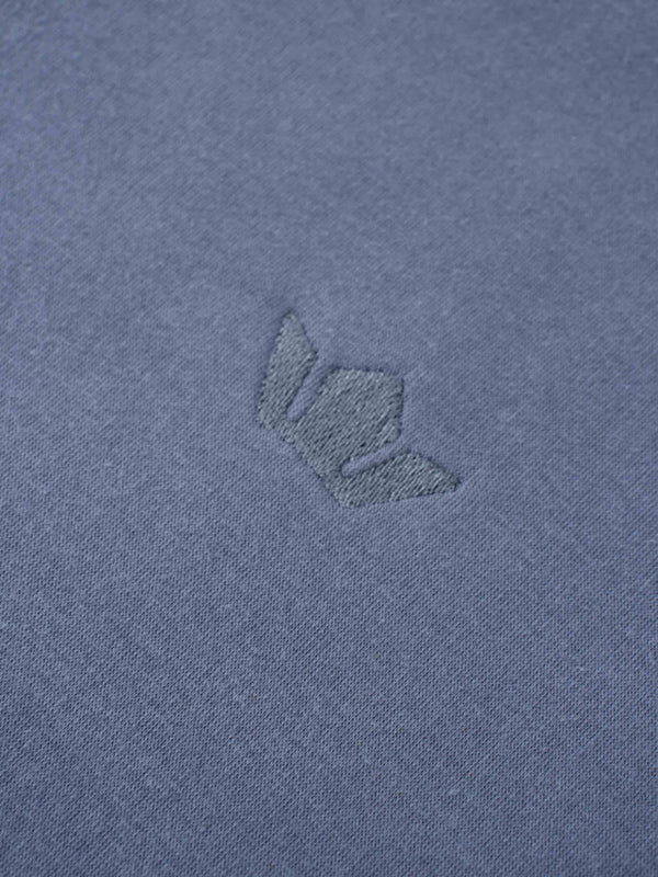 A full, front view of the dusty-blue sweatshirt. It has a ribbed crewneck collar, cuffs, and bottom hem, with the small, tone-on-tone embroidered logo visible on the left chest.