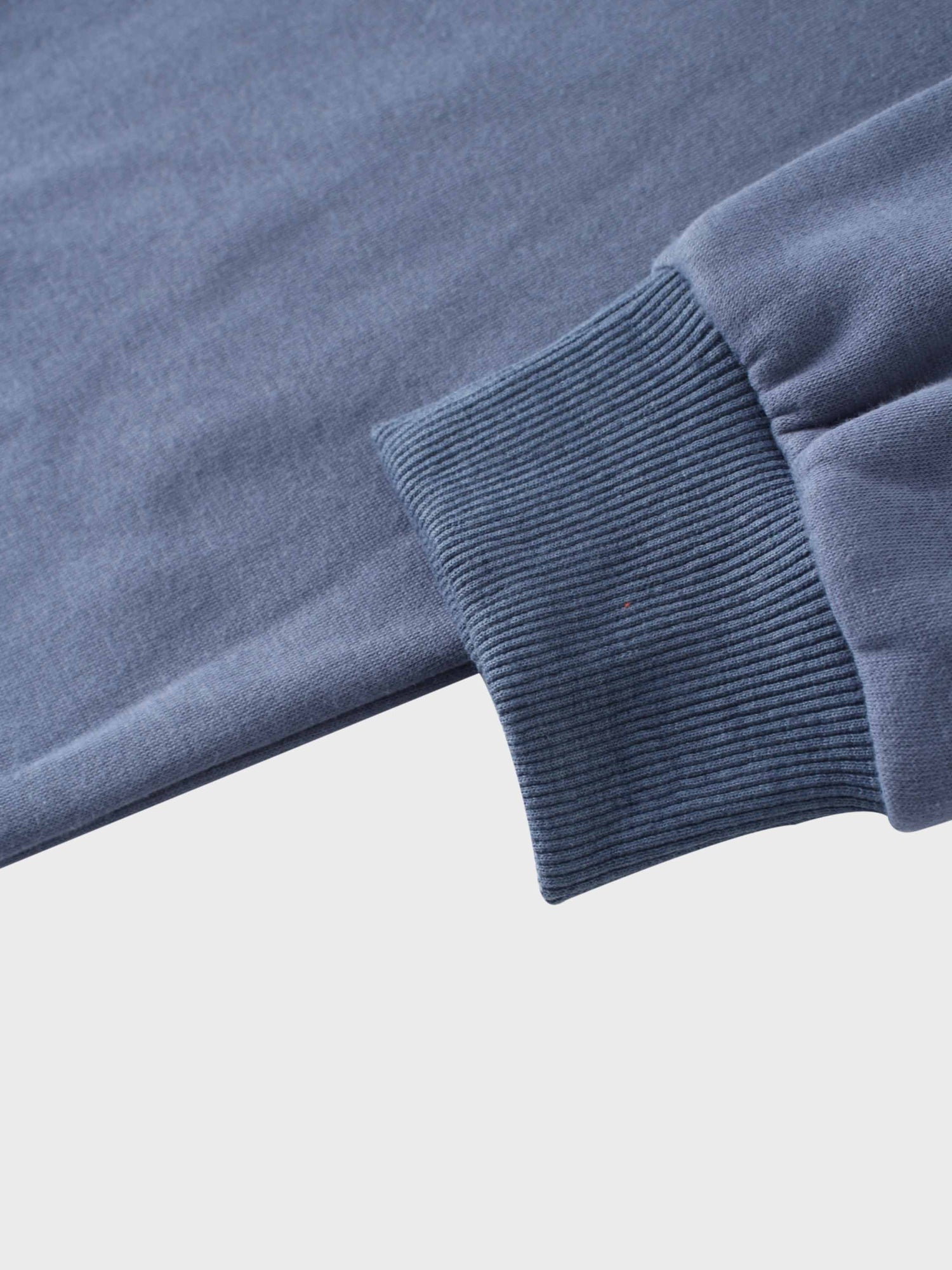 A close-up view of a sleeve, showing the contrast in texture between the smooth, dusty-blue fabric of the arm and the thick, stretchy ribbed cuff at the wrist.