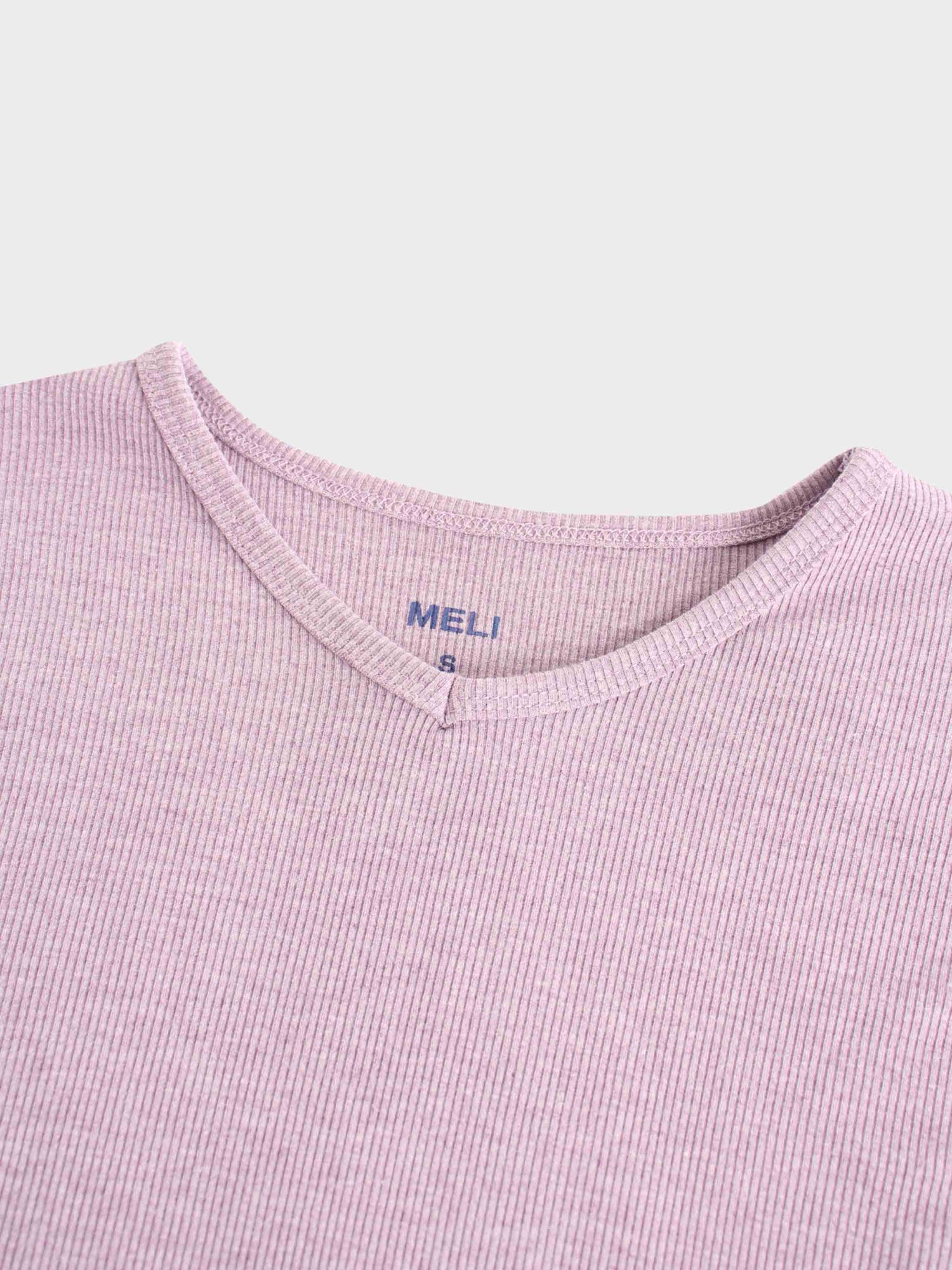A close-up of the notched neckline on the lavender ribbed shirt. A tag printed in blue on the inside reads &quot;MELI&quot; with the size &quot;S&quot; below it.