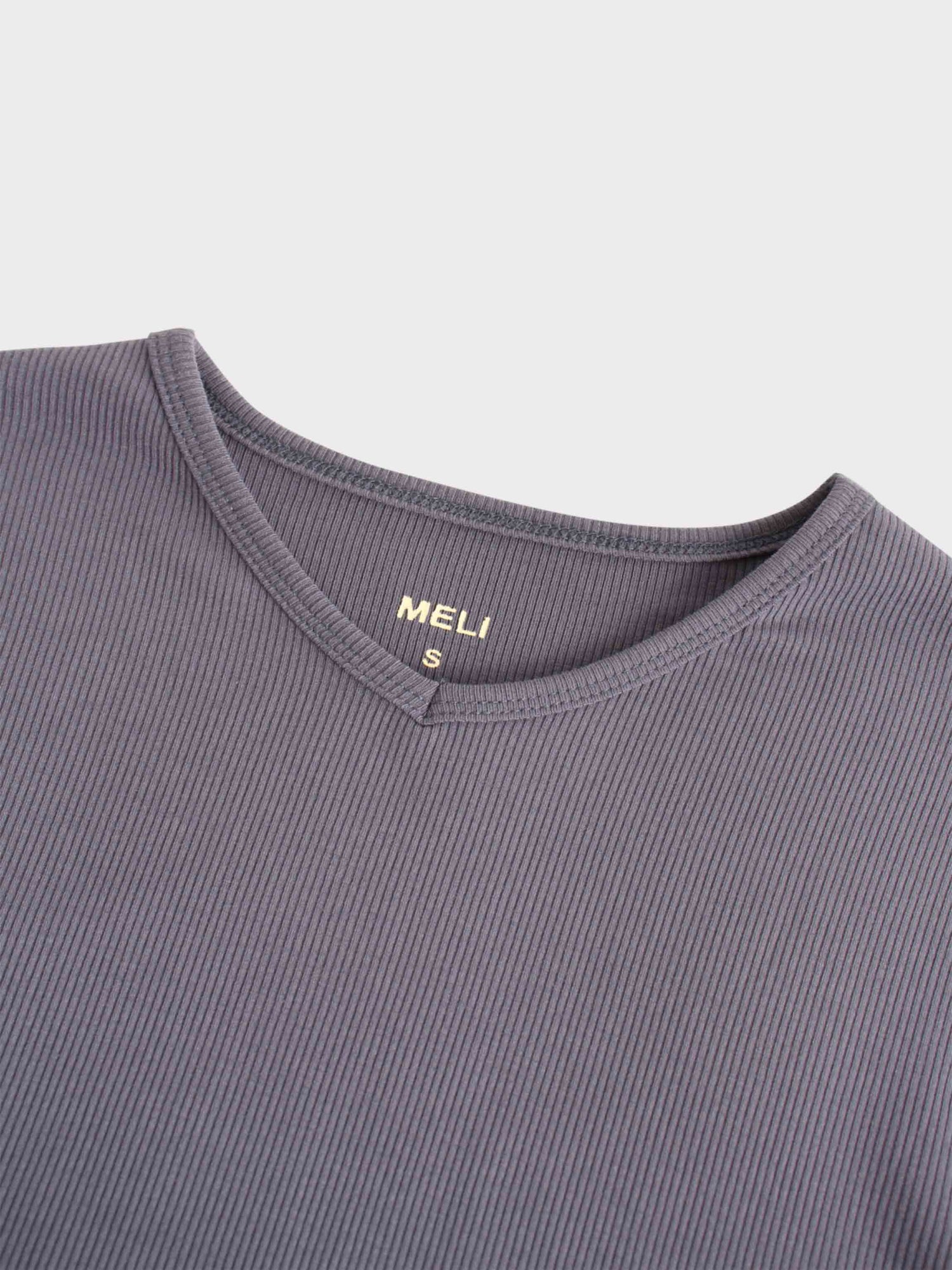 A view of the neckline of the ribbed, purple shirt. It has a small V-shaped notch at the front, and a tag printed in gold on the inside reads &quot;MELI&quot; with an &quot;S&quot; for the size.